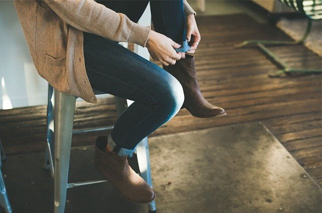 Girl in jeans sitting on a high chair and putting her boots on, an example of what to wear on a moving day