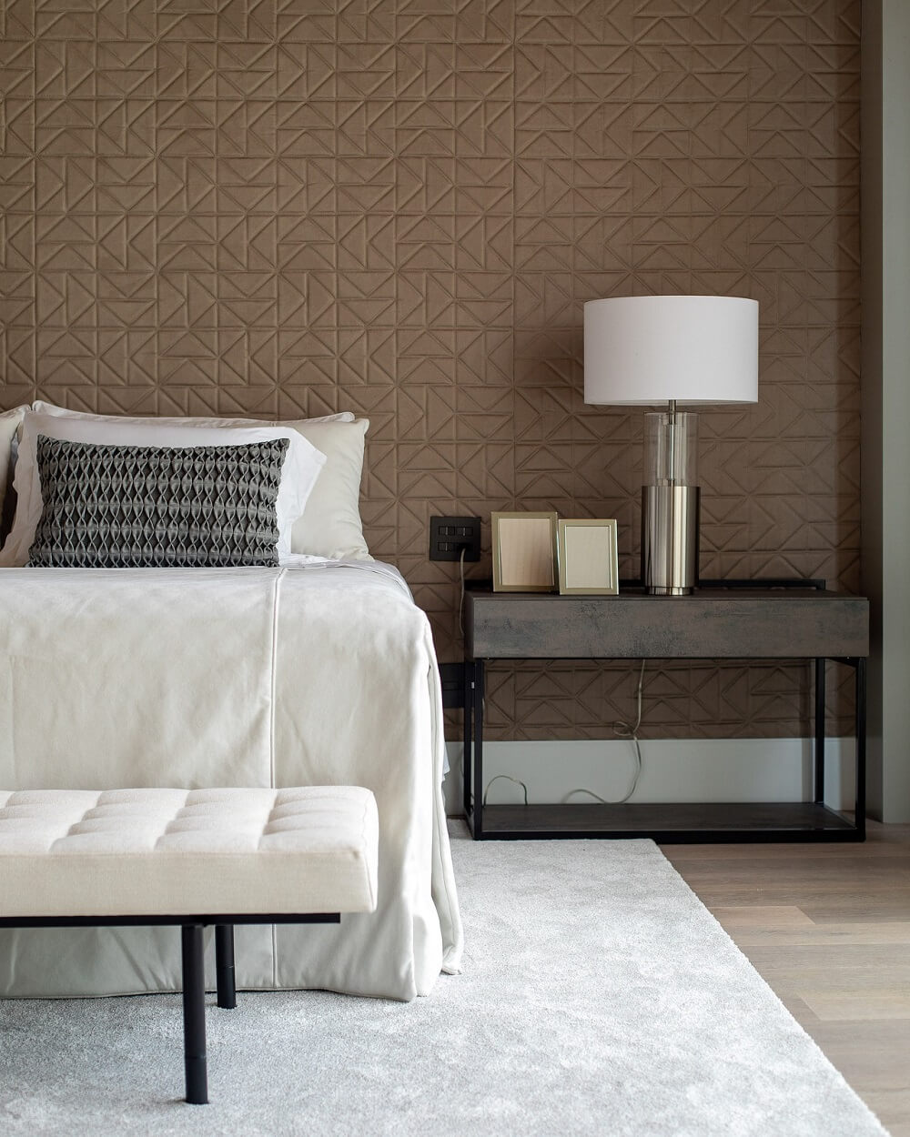 A white bed with white sheets, brown details and an elegant lamp