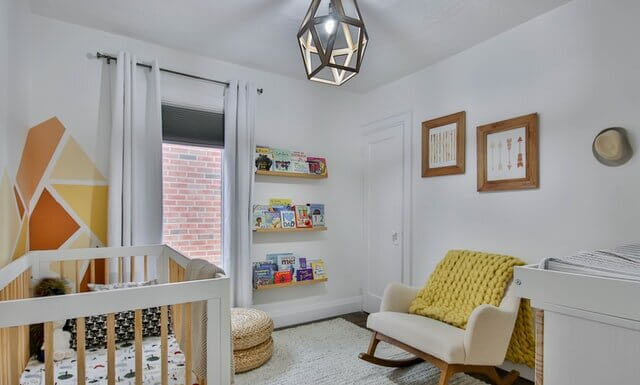 DIY Nursery Decor Tips A nursery painted white with a chair, bookshelf and two paintings on the wall.
