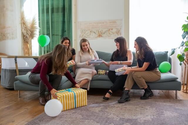 A woman opening a gift at her baby shower with four friends sitting next to her.